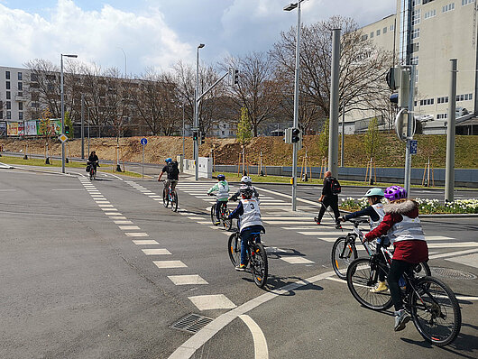 eine Gruppe von Kindern in Begleitung der Trainer fährt über eine Radfahrerüberfahrt mit Ampel